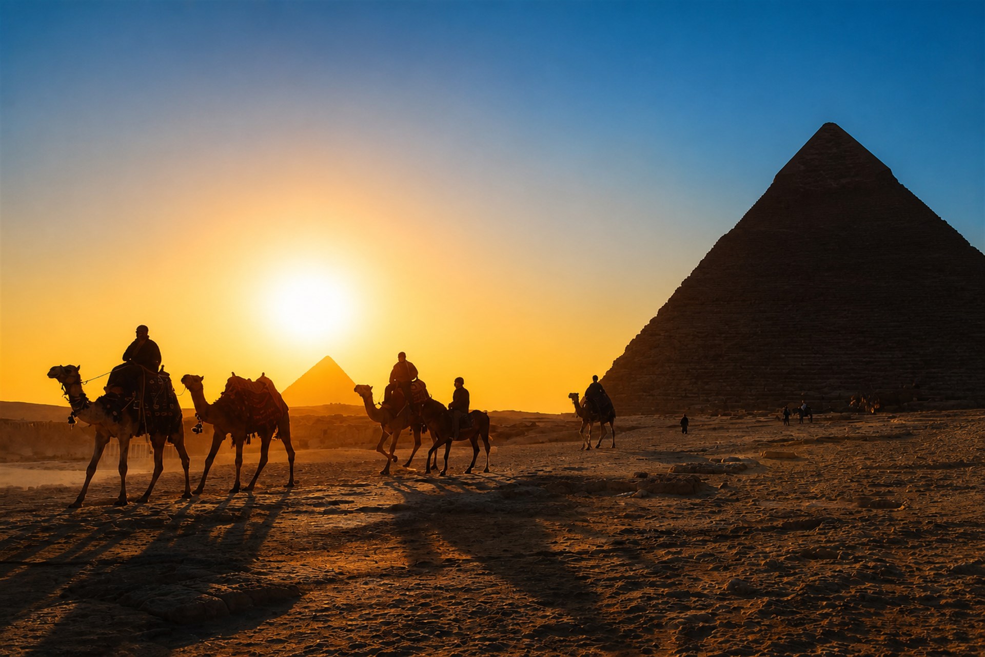 Camel riders and the pyramids at sunset